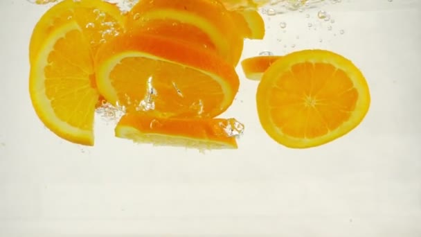 Sappige stukjes sinaasappel vallen in water met spatten en bubbels, Slowmotion close-up — Stockvideo