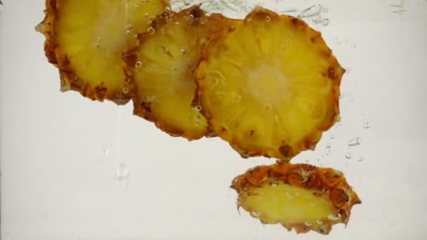 Сочные кусочки ананаса падают в воду со следом из пузырьков, замедленное движение крупным планом — стоковое видео