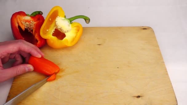 Oranje chilipeper snijden met een mes op een houten bord — Stockvideo