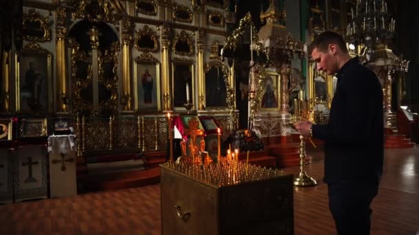 Elets, Russian Federation - April 2, 2018: Ένας άνδρας με μαύρα ρούχα ανάβει ένα κερί στο ναό. — Αρχείο Βίντεο