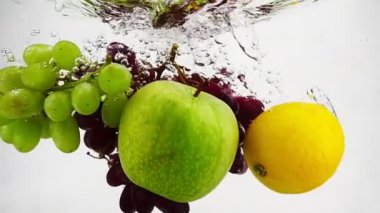 Limon, elma ve üzümler kabarcıklarla suya düşüyor. Ağır çekimde video. İzole edilmiş beyaz arkaplanda meyveler.