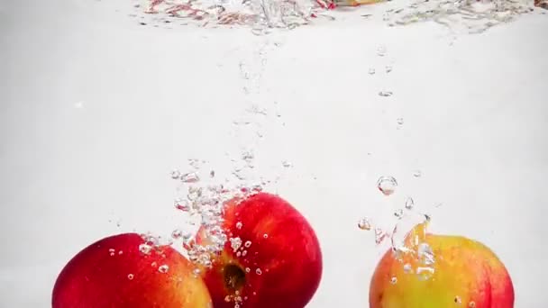 Las manzanas rojas maduras caen en el agua con burbujas. Vídeo en movimiento lento. — Vídeo de stock