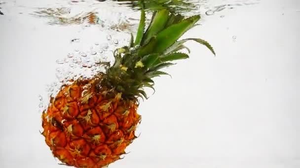 Ananas powoli tonie w wodzie z falami i bąbelkami. — Wideo stockowe