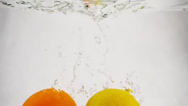 明るいレモンとオレンジの泡が水に落ちる。孤立した白い背景にスローモーションで柑橘系のフルーツ. — ストック動画