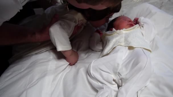 Маленькая кавказская сестра целует новорожденного брата, спящего на кровати — стоковое видео