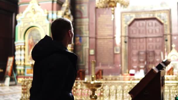 Um homem olha para a luz na Igreja Ortodoxa — Vídeo de Stock