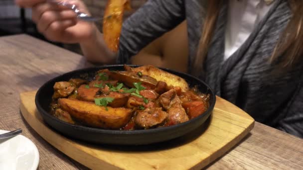 Woman eats fried potato served on pan on wood board in cafe, hands closeup. — Stock Video