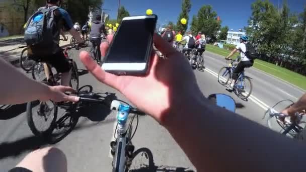 Велосипедист смотрит на телефон езда велосипеда среди группы велосипедистов, видео от первого лица . — стоковое видео