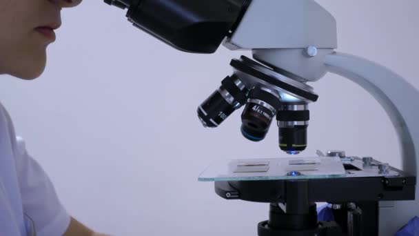 Técnico de laboratorio mujer mira fijamente en los oculares de un microscopio — Vídeos de Stock