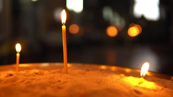 Три горящие свечи различной длины, стоящие в песке — стоковое видео
