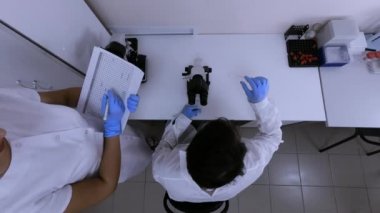 İki laboratuvar asistanı mikroskoplu bilimsel bir laboratuvarda çalışıyor.
