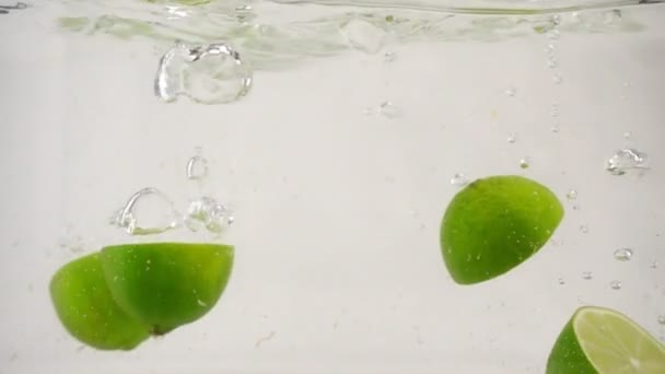 Saftige Lyme-Hälften fallen mit Blasen und Spritzern ins Wasser, Zeitlupe Nahaufnahme — Stockvideo