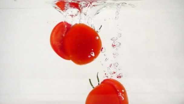 Gesneden tomaten vallen in het water met spatten en bubbels, Slow Motion close-up — Stockvideo