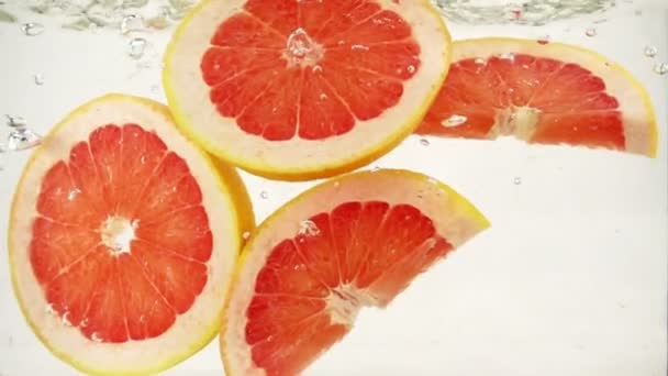 Grapefruit szeletek esnek a vízbe, lassú mozgás közelről — Stock videók