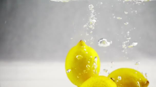 Citrons jaunes brillants tombant dans l'eau au ralenti. Fruits sur fond blanc isolé . — Video