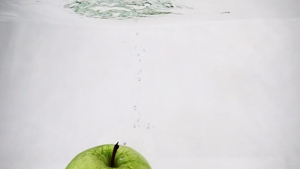 Do vody s bublinkami se vhazuje zelené šťavnaté jablko. Pomalý pohyb videa. — Stock video