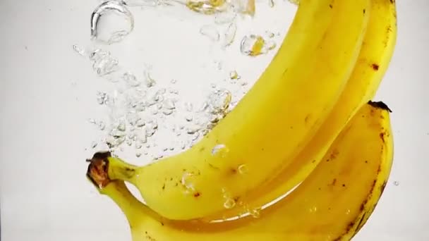 De mogna bananer faller i vattnet med stänk och bubblor i slow motion. — Stockvideo