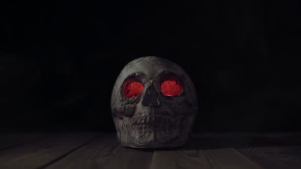 Старый человеческий череп со светящимися глазами в дыму на деревянном столе — стоковое видео