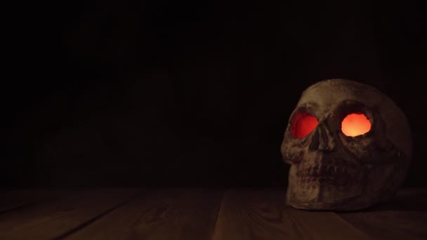 Mann platziert auf Holztisch menschlichen alten Schädel mit leuchtenden Augen und kommt aus ihnen heraus in Rauch — Stockvideo