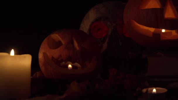 Dos calabazas con caras talladas y un cráneo a la luz de las velas, video en bucle — Vídeo de stock