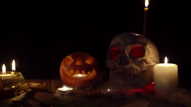 A human skull and a pumpkin with a face stand on table in a cloud of smoke — Stock Video