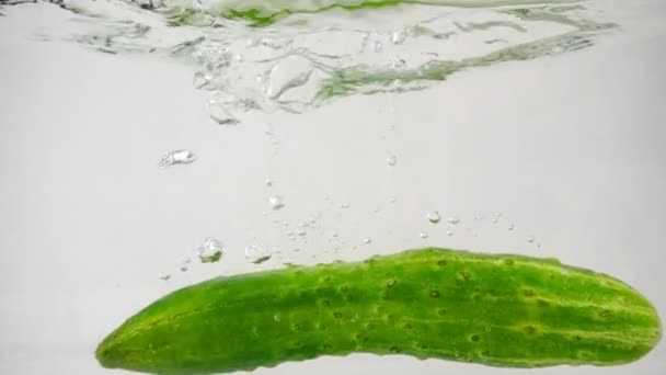 Zielony świeży ogórek wpada do wody z rozpryskami i bąbelkami — Wideo stockowe