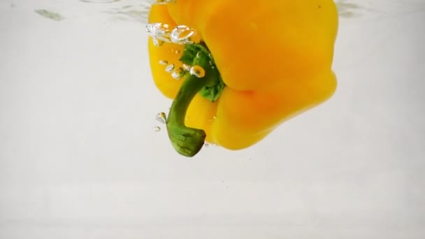 Un pimiento fresco de pimentón amarillo cae al agua en el centro con salpicaduras y burbujas — Vídeo de stock