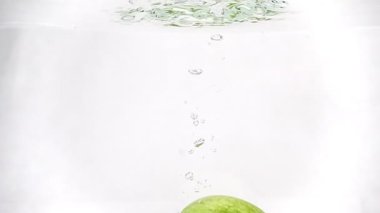 Yeşil elma yavaşça suya battı. Ağır çekimde video. Beyaz arka planda izole meyveler.