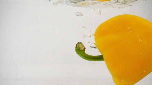 Un pimiento amarillo pimentón dulce cae en el agua a la derecha con salpicaduras y burbujas — Vídeos de Stock