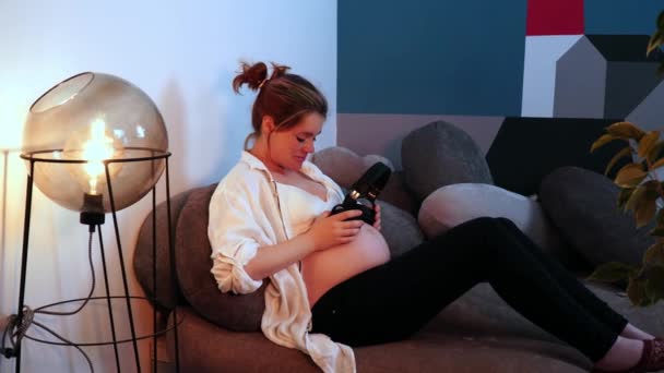 Mujer embarazada está sentada y deja que su vientre escuche música en los auriculares — Vídeo de stock