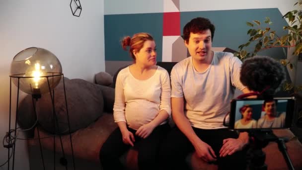 Чоловік і вагітна жінка сидять і розмовляють з камерою телефону — стокове відео