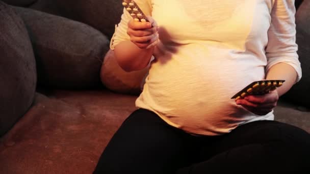 Gravid kvinna försöker välja mellan två piller och axelryckningar axlar — Stockvideo