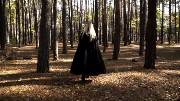 Şişko sarışın aktris sonbahar ormanlarında siyah pelerinli yürüyor. — Stok video