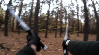 Deri eldivenli siyah kollu Larp oyuncusu iki kılıç çeviriyor.