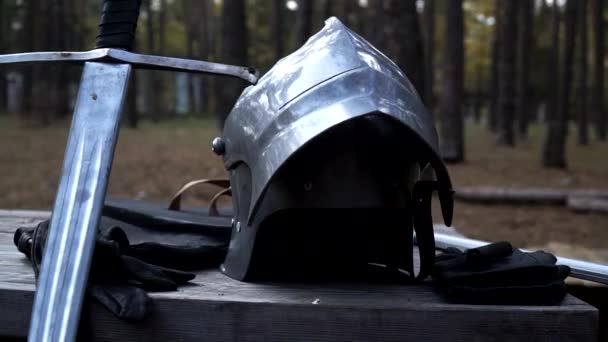 IJzeren helm, zwaard en leren handschoenen staan aan de houten tafel — Stockvideo