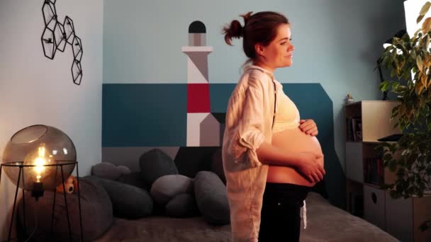 Giovane futura madre in camicia bianca sta accarezzando la pancia fissando avanti — Video Stock