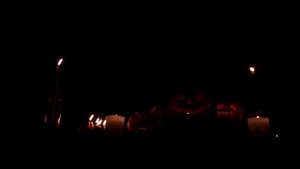 Composition Jacks lanterns between candles on a black background in slow motion — Stock Video