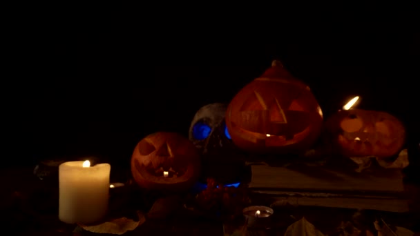 Un cráneo humano y tres linternas Jack con velas en el interior sobre un fondo negro, video en bucle — Vídeo de stock