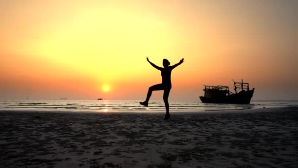Σιλουέτα ενός κοριτσιού που χοροπηδάει χαρούμενα στο ηλιοβασίλεμα στον ωκεανό κοντά στο πλοίο — Αρχείο Βίντεο