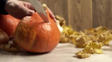 Kız, balkabağına bıçak saplar. Ahşap bir arka plana yakın durur.