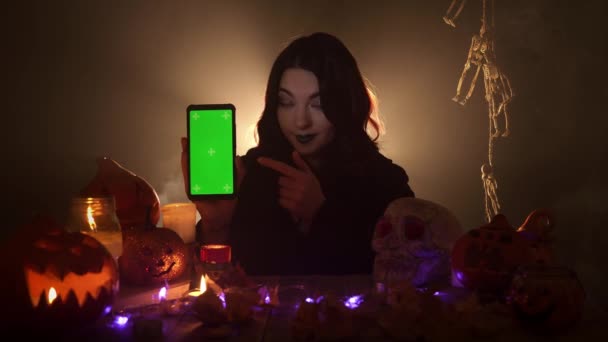 The woman is holding cellphone with green screen in her hand and points it — Stock Video