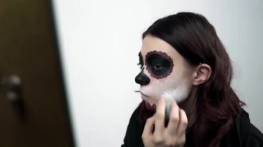 Kız yüzünü beyaza boyuyor. Santa Muerte bayramı için geleneksel bir makyaj.