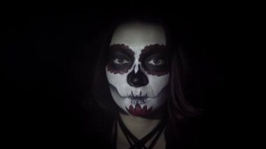 Dinamik bir spot ışığında geleneksel Santa Muerte makyajlı bir kızın portresi.