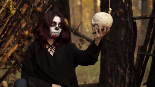 Girl with Santa Muerte makeup holds a skull in her hands and strokes it in nature — Stock Video