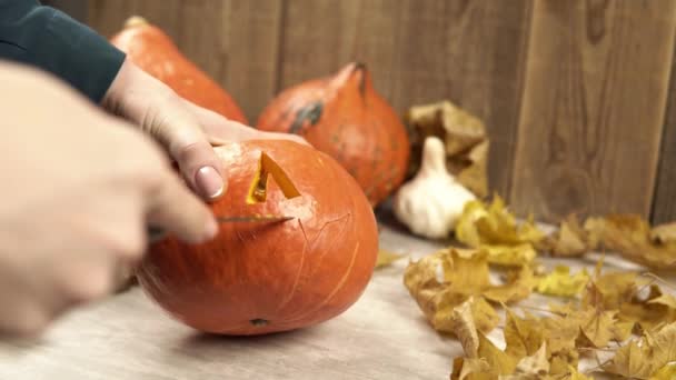 Vrouw houdt halloween pompoen en snijdt de mond met behulp van scherp mes — Stockvideo