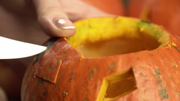 Woman uses sharp knife to remove a piece of pumpkin to make en eye — Stock Video