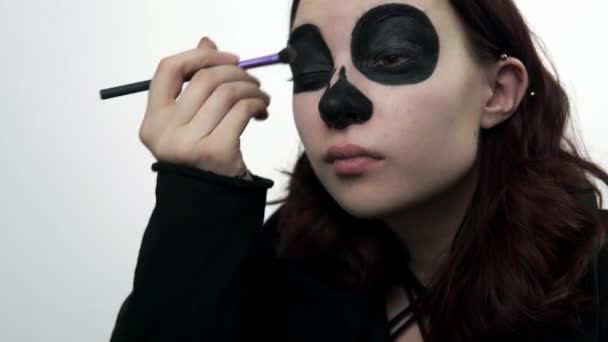 Young woman uses brush to apply eyeshadows for santa muerte makeup — Stock Video