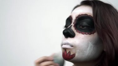 Kadın, Noel Baba makyajı için yüzüne süngerle beyaz boya sürüyor.