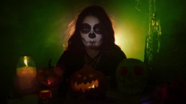 Santa Muerte makyajlı bir kız balkabağı tutuyor ve ileriye taşıyor.