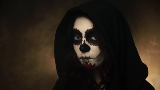Menina de capuz preto e maquiagem santa muerte vira a cabeça e assiste em linha reta — Vídeo de Stock